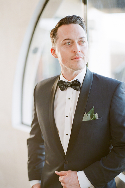 Los angeles same sex outdoor wedding at malibu solstice canyon groom navy shawl lapel tuxedo with a white dress shirt and black and white dot bow tie with greenery pocket boutonniere