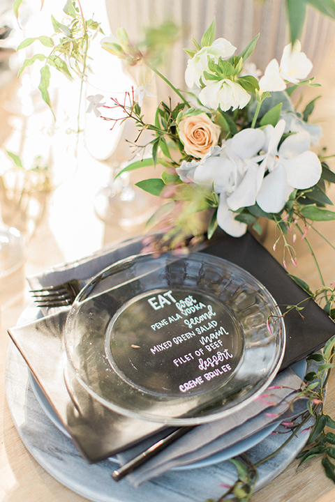 Los angeles same sex wedding at malibu solstice canyon table set up light brown wood table with white chairs and white and green flower centerpiece decor with white candles in glass vases and clear glass plates wedding photo idea close up on place setting