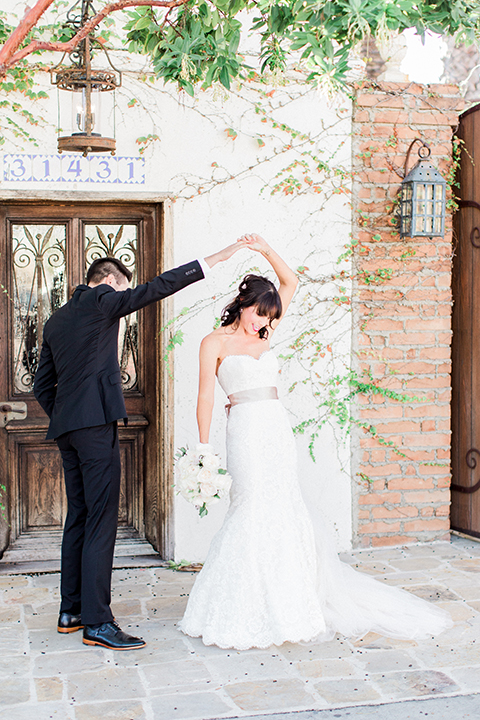 Fall wedding at the villa san juan capistrano bride strapless mermaid fit gown with a sweetheart neckline and ribbon belt with bow in the back with groom black notch lapel suit with a white dress shirt and black bow tie with a black and white plaid pocket square and white floral boutonniere first look bride and groom dancing bride holding white floral bridal bouquet