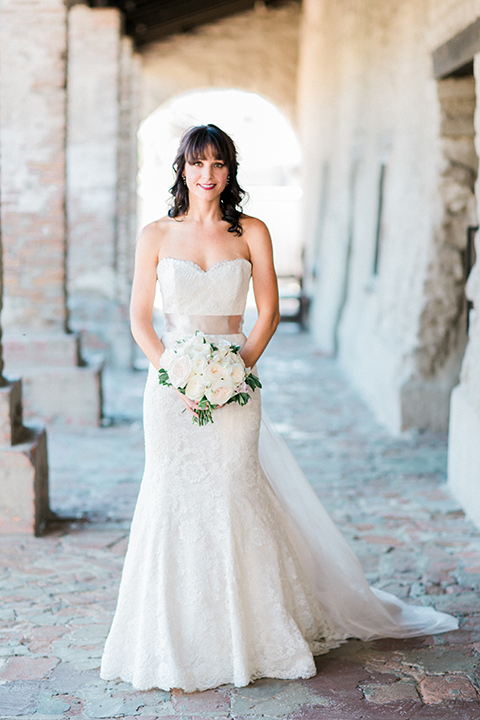 Fall wedding at the villa san juan capistrano bride strapless mermaid fit gown with a sweetheart neckline and ribbon belt with bow in the back holding white floral bridal bouquet smiling
