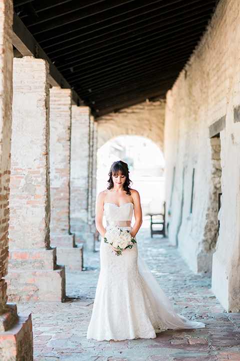 Fall wedding at the villa san juan capistrano bride strapless mermaid fit gown with a sweetheart neckline and ribbon belt with bow in the back holding white floral bridal bouquet