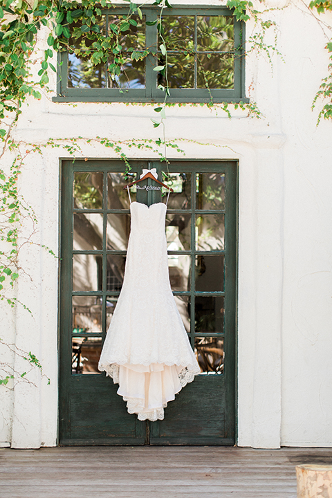 Fall wedding at the villa san juan capistrano bride strapless mermaid fit gown with a sweetheart neckline and ribbon belt with bow in the back hanging on hanger outside door wedding photo idea of brides dress
