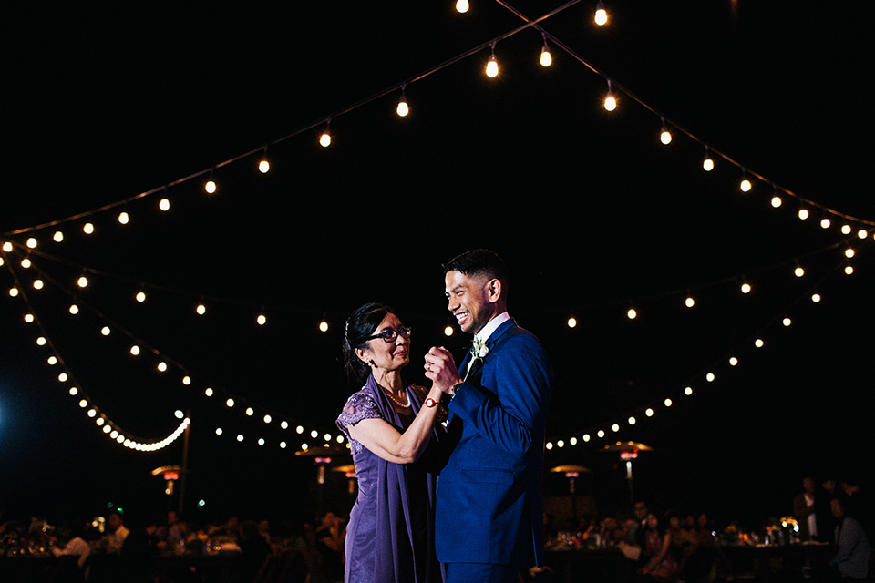 San diego autumn inspired outdoor wedding at limoneira ranch groom cobalt blue notch lapel suit with a matching vest and white dress shirt with a long white tie and white floral boutonniere dancing with mom at reception