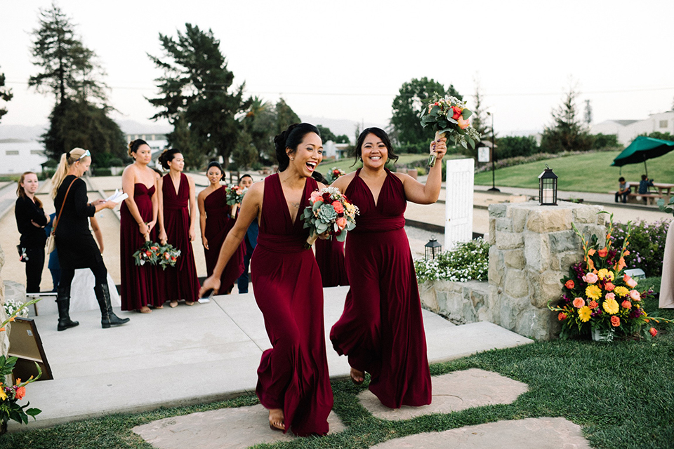 San diego autumn inspired outdoor wedding at limoneira ranch reception wedding party entrance bridesmaids long burgundy dresses holding green and red floral bouquets walking in together