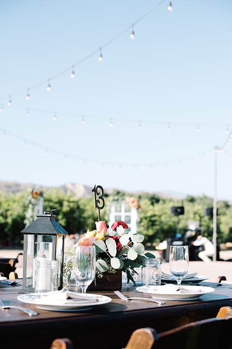 San diego autumn inspired outdoor wedding at limoneira ranch table set up light blue table linen with light orange and green flower centerpiece decor with light brown wooden rustic chairs and lantern and candle decor with table number in flowers