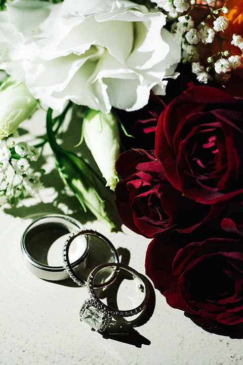 San diego autumn inspired outdoor wedding at limoneira ranch wedding rings for bride and groom on white linen with dark red roses and white flower decor on light background wedding photo idea for wedding rings