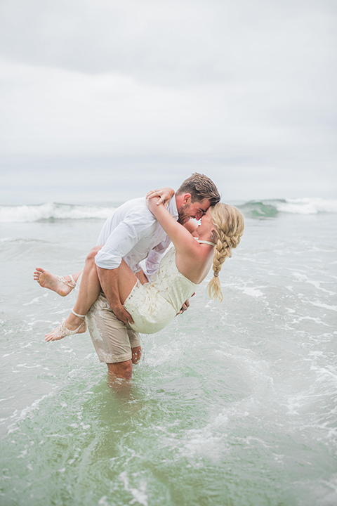 San diego beach wedding at blacks beach bride strapless ball gown with a sweetheart neckline and crystal belt and headband with groom light grey peak lapel suit by ike behar with a matching vest and white dress shirt with a long red matte tie and red flower lapel pin in the water hugging and touching heads