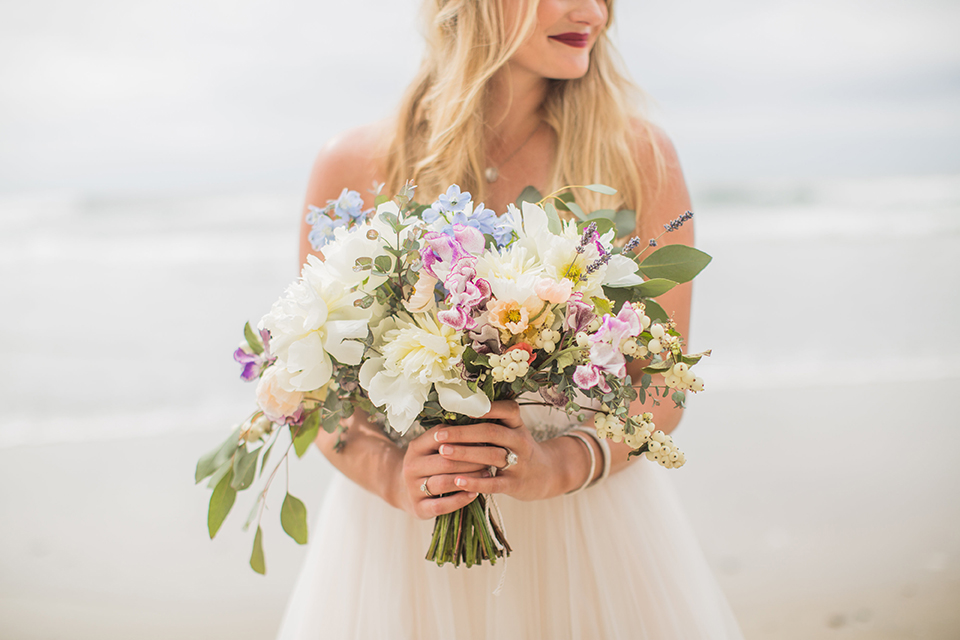 San diego beach wedding at blacks beach bride strapless ball gown with a sweetheart neckline and crystal belt and headband holding light pink and blue floral bridal bouquet close up on bouquet