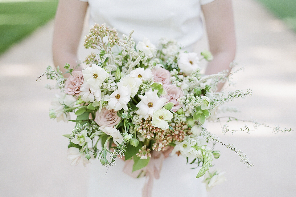 Santa barbara outdoor black tie wedding at kestrel park bride simple form fitting gown with a high neckline and short sleeves holding white and green floral bridal bouquet close up on bouquet