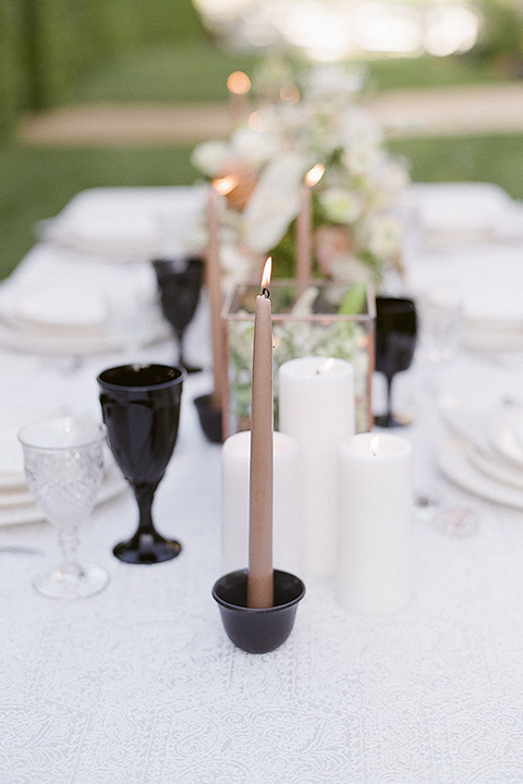 Santa barbara outdoor black tie wedding at kestrel park table set up with white lace linen and white place settings with white linen napkins and black wine glasses with white and green floral centerpiece decor with black and gold candles and wooden rustic chairs