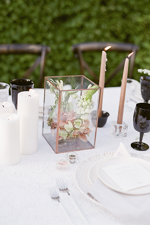 Santa barbara outdoor black tie wedding at kestrel park table set up with white lace linen and white place settings with white linen napkins and black wine glasses with white and green floral centerpiece decor with black and gold candles and wooden rustic chairs