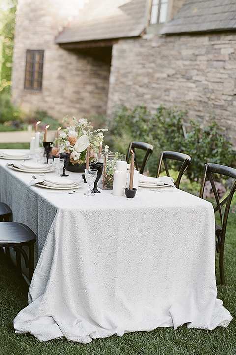 Santa barbara outdoor black tie wedding at kestrel park table set up with white lace linen and white place settings with white linen napkins and black wine glasses with white and green floral centerpiece decor with black and gold candles and wooden rustic chairs