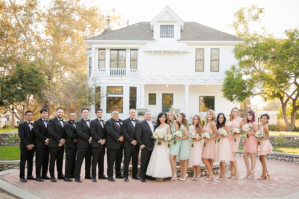 Orange county outdoor summer wedding at the heritage museum bride ball gown with lace straps and a sweetheart neckline with a short tulle skirt and long veil with groom black shawl lapel tuxedo with a white dress shirt and white vest with a white tie and white floral boutonniere standing with wedding party