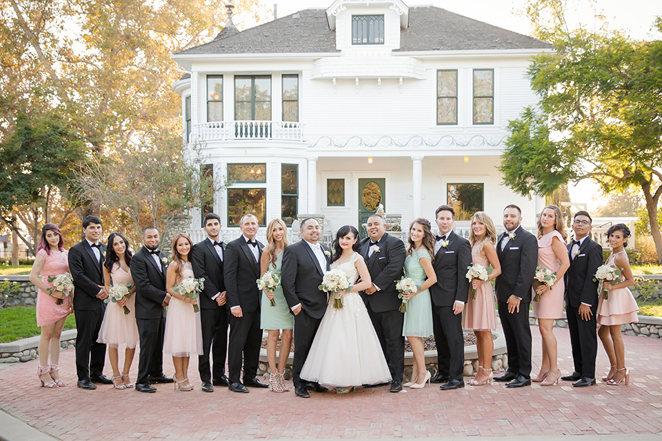 Orange county outdoor summer wedding at the heritage museum bride ball gown with lace straps and a sweetheart neckline with a short tulle skirt and long veil with groom black shawl lapel tuxedo with a white dress shirt and white vest with a white tie and white floral boutonniere standing with wedding party