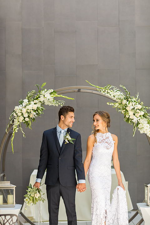 San diego wedding at the hilton bayside bride form fitting lace halter gown with a high neckline design and groom navy blue notch lapel suit with a matching vest and light blue dress shirt with a long blue tie and white and green floral boutonniere holding hands