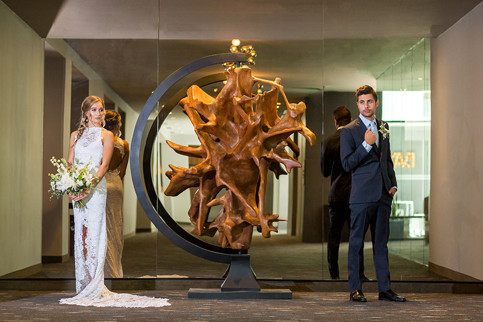 San diego wedding at the hilton bayside bride form fitting lace gown with high neckline and floral bridal bouquet with groom navy notch lapel suit with matching vest and white dress shirt with long blue tie standing