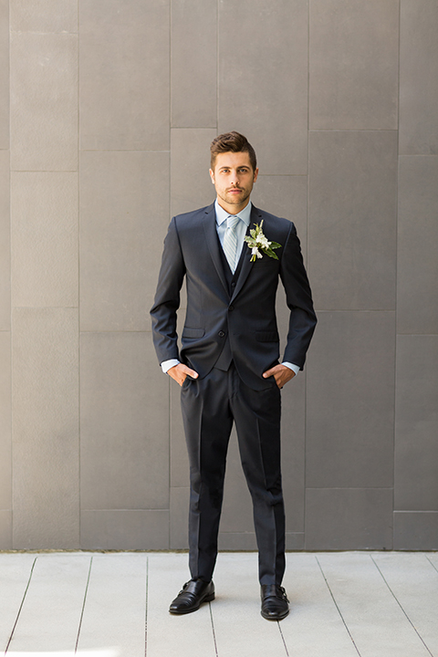San diego wedding at the hilton bayside groom navy notch lapel suit with a matching vest and white dress shirt with a long blue tie standing with hands in pockets