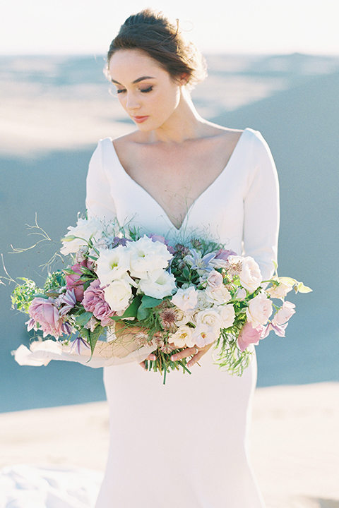 California outdoor wedding shoot at glamis sand dunes bride form fitting long sleeved gown with an open back design and plunging neckline with low hair updo holding white and light pink floral bridal bouquet close up