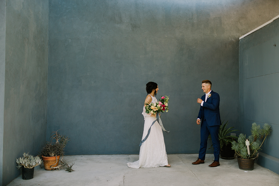 Los angeles outdoor colorful wedding bride a line gown with a high neckline and open shoulder lace sleeves and groom cobalt blue notch lapel suit by allure men with a matching vest and white dress shirt with a long white matte tie and white floral boutonniere first look groom smiling