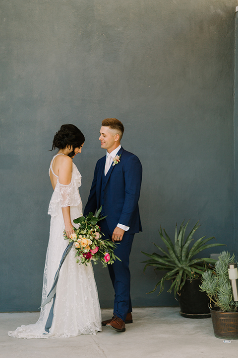 Los angeles outdoor colorful wedding bride a line gown with a high neckline and open shoulder lace sleeves and groom cobalt blue notch lapel suit by allure men with a matching vest and white dress shirt with a long white matte tie and white floral boutonniere holding hands and bride holding colorful floral bridal bouquet