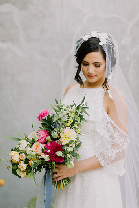 Los angeles outdoor colorful wedding bride a line gown with a high neckline and open shoulder lace sleeves with long veil and lace detail holding colorful floral bridal bouquet with long blue ribbon close up