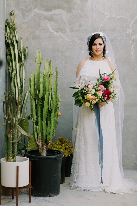 Los angeles outdoor colorful wedding bride a line gown with a high neckline and open shoulder lace sleeves with long veil and lace detail holding colorful floral bridal bouquet with long blue ribbon 