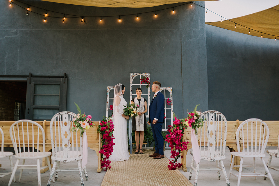 Los angeles outdoor colorful wedding bride a line gown with a high neckline and open shoulder lace sleeves and groom cobalt blue notch lapel suit by allure men with a matching vest and white dress shirt with a long white matte tie and white floral boutonniere standing during ceremony