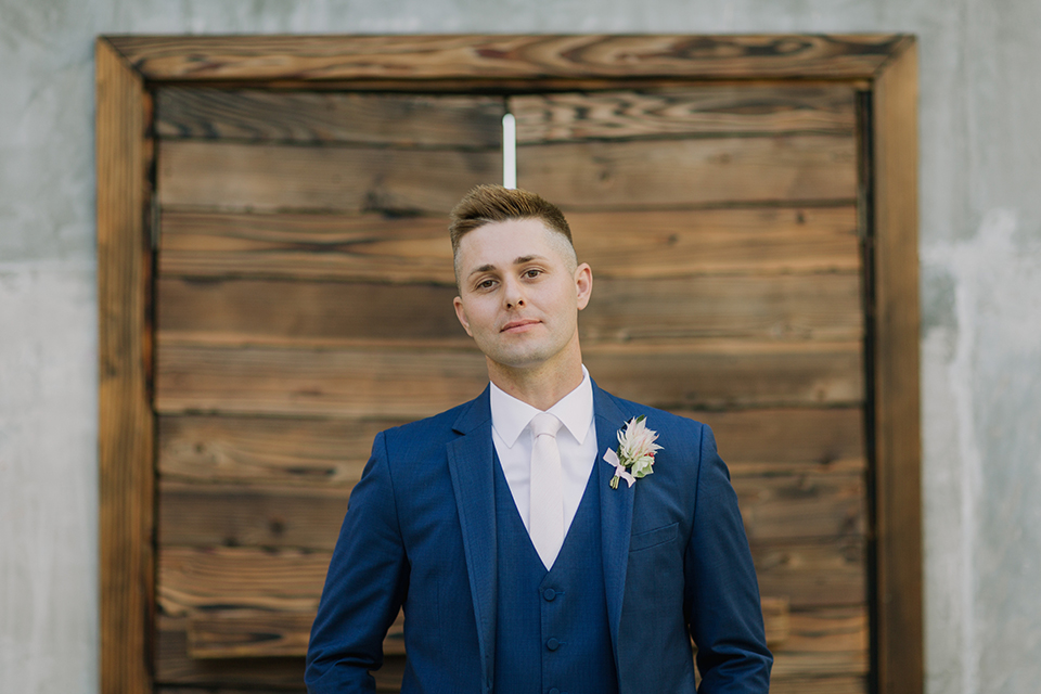 Los angeles outdoor colorful wedding at city libre groom cobalt blue notch lapel suit by allure men with a matching vest and a white dress shirt with a long white matte tie and white floral boutonniere standing with hands in pockets close up