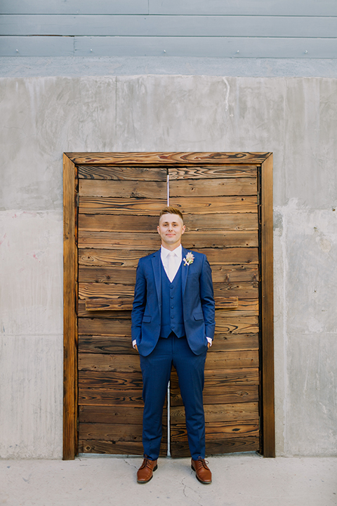 Los angeles outdoor colorful wedding at city libre groom cobalt blue notch lapel suit by allure men with a matching vest and a white dress shirt with a long white matte tie and white floral boutonniere standing with hands in pockets