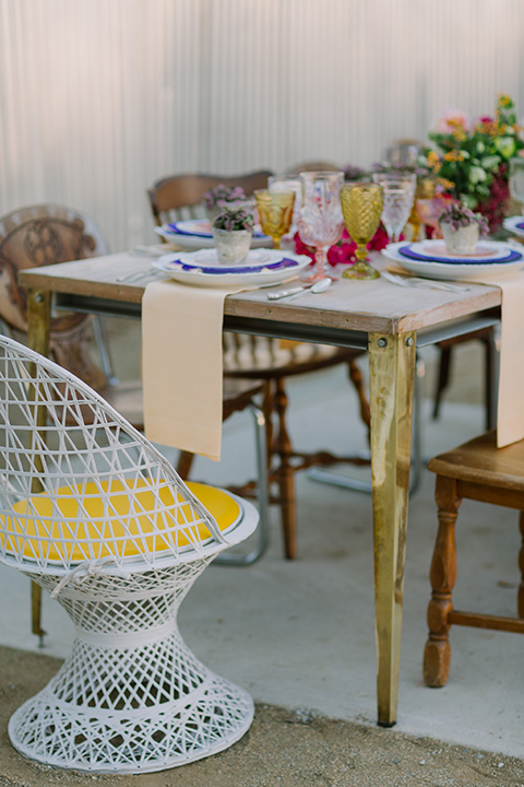 Los angeles outdoor colorful wedding at city libre table set up light brown wood table with an assortment of different style wooden chairs and flower centerpiece decor with white and blue place settings and colorful glassware