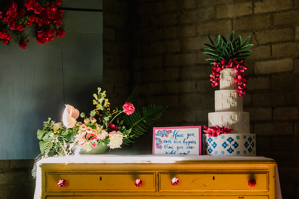 Los angeles outdoor colorful wedding at city libre wedding dessert table set up light brown wooden table with drawers and four tier white and blue wedding cake with bright pink florals on top with calligraphy sign and flower decor on top of table wedding photo idea for dessert table and wedding cake