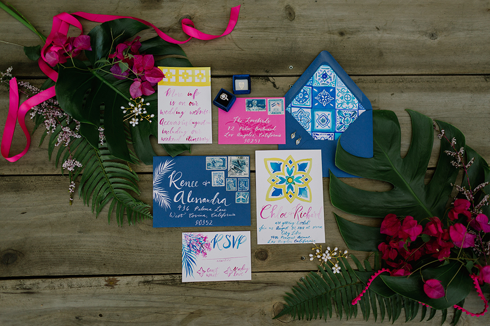 Los angeles outdoor colorful wedding at city libre wedding invitations white invitations with bright pink writing and colorful designs with blue patterned envelopes and bright pink and green florals on light brown wooden background wedding photo idea for invitations