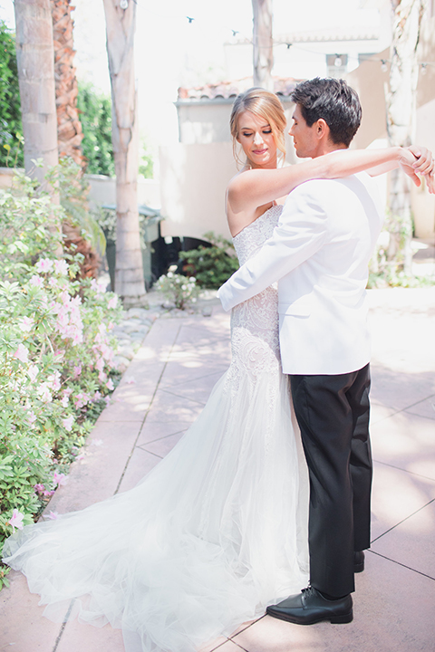 Pasadena outdoor wedding at the maxwell house bride mermaid style gown with thin spaghetti straps and beaded detail with a sweetheart neckline and groom white dinner jacket with black tuxedo pants and a white dress shirt with a black bow tie hugging