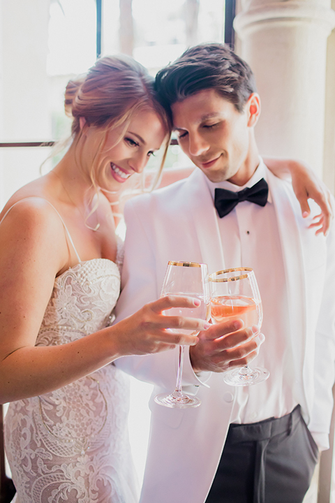 Pasadena outdoor wedding at the maxwell house bride mermaid style gown with thin spaghetti straps and beaded detail with a sweetheart neckline and groom white dinner jacket with black tuxedo pants and a white dress shirt with a black bow tie standing and hugging holding drinks