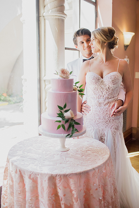 Pasadena outdoor wedding at the maxwell house bride mermaid style gown with thin spaghetti straps and beaded detail with a sweetheart neckline and groom white dinner jacket with black tuxedo pants and a white dress shirt with a black bow tie standing by cake hugging