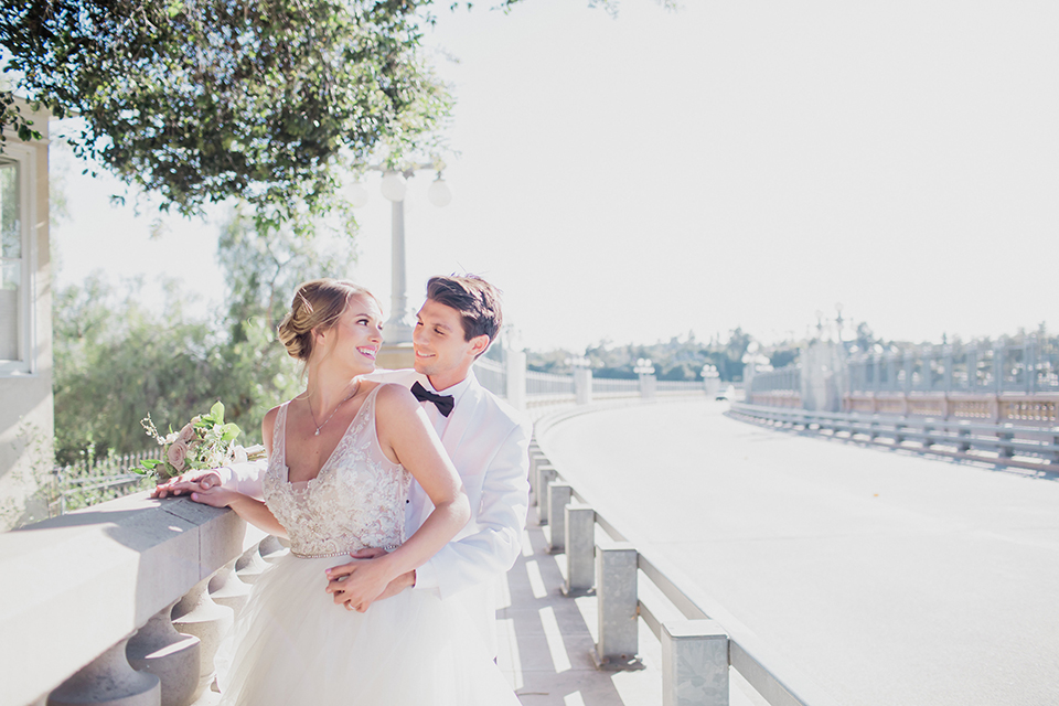 Pasadena outdoor wedding at the maxwell house bride mermaid style gown with thin spaghetti straps and beaded detail with a sweetheart neckline and groom white dinner jacket with black tuxedo pants and a white dress shirt with a black bow tie hugging