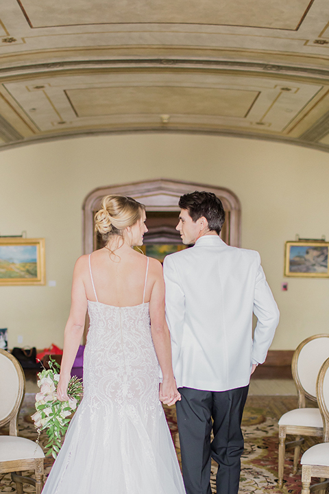 Pasadena outdoor wedding at the maxwell house bride mermaid style gown with thin spaghetti straps and beaded detail with a sweetheart neckline and groom white dinner jacket with black tuxedo pants and a white dress shirt with a black bow tie holding hands and walking down aisle after ceremony