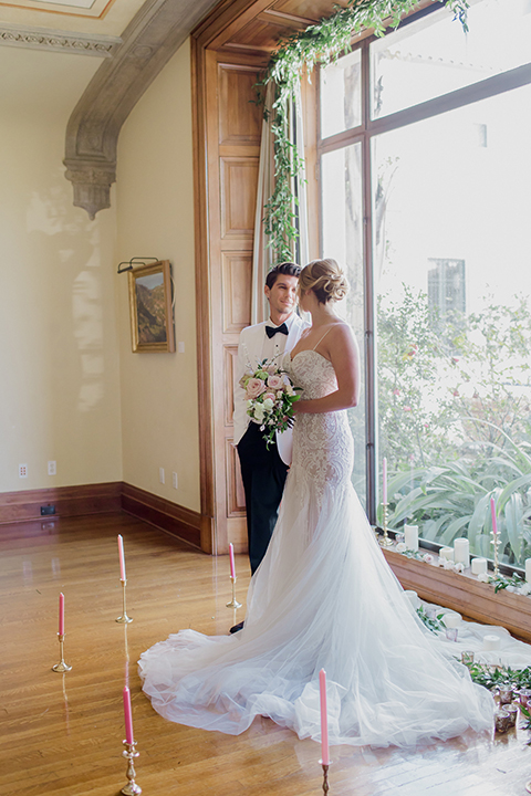 Pasadena outdoor wedding at the maxwell house bride mermaid style gown with thin spaghetti straps and beaded detail with a sweetheart neckline and groom white dinner jacket with black tuxedo pants and a white dress shirt with a black bow tie holding hands during ceremony