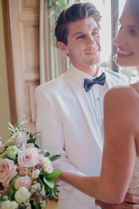 Pasadena outdoor wedding at the maxwell house bride mermaid style gown with thin spaghetti straps and beaded detail with a sweetheart neckline and groom white dinner jacket with black tuxedo pants and a white dress shirt with a black bow tie hugging during ceremony close up