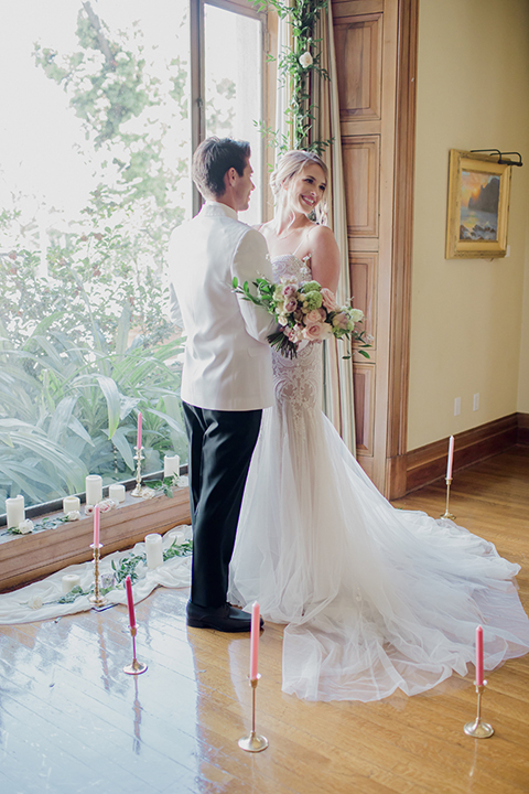 Pasadena outdoor wedding at the maxwell house bride mermaid style gown with thin spaghetti straps and beaded detail with a sweetheart neckline and groom white dinner jacket with black tuxedo pants and a white dress shirt with a black bow tie hugging during ceremony 