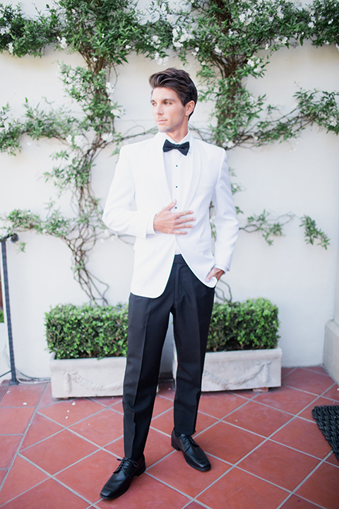 Pasadena outdoor wedding at the maxwell house groom white dinner jacket with black tuxedo pants and a white dress shirt with a black bow tie standing holding jacket