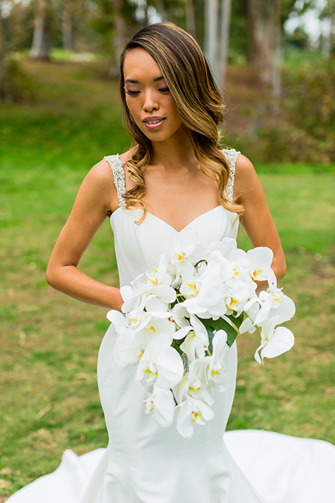 Southern california outdoor wedding at diamond bar golf course bride form fitting mermaid style gown with silver beaded straps and a sweetheart neckline with a low back design and beaded detail with white and green floral bridal bouquet close up