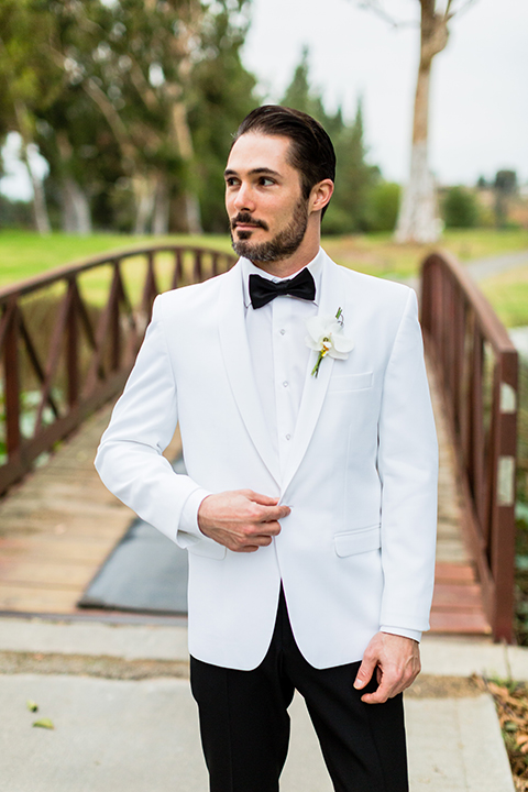 Southern california outdoor wedding at diamond bar golf course groom white notch lapel dinner jacket with a white dress shirt and black tuxedo pants with a black bow tie and white floral boutonniere holding jacket