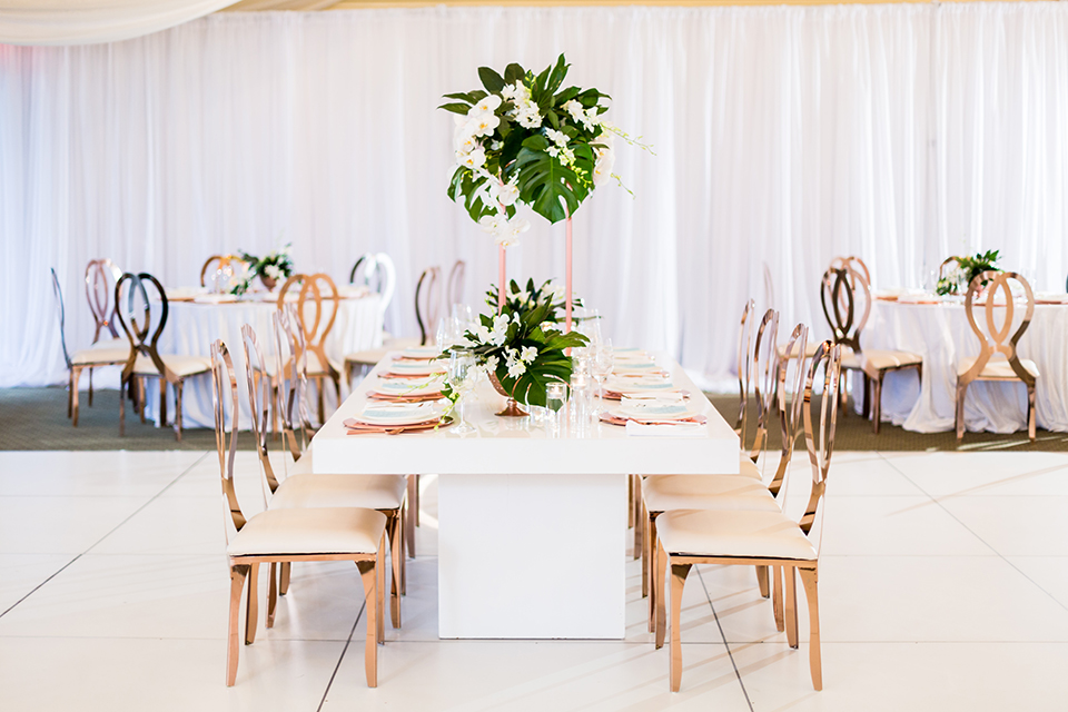Southern california outdoor wedding at diamond bar golf course table set up white table with greenery floral decor and rose gold chairs with hanging decor and wall with greenery florals and white and gold place settings with gold silverware