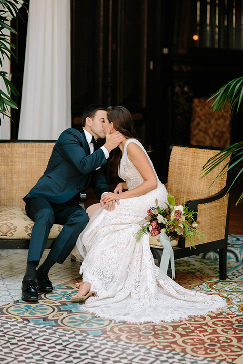 Southern-california-wedding-at-the-ebell-of-long-beach-bride-and-groom-holding-hands-sitting-and-kissing-bride-wearing-a-lace-a-line-dress-with-straps-and-hair-in-loose-down-waves-and-groom-in-navy-tux-with-black-trim-and-black-bowtie