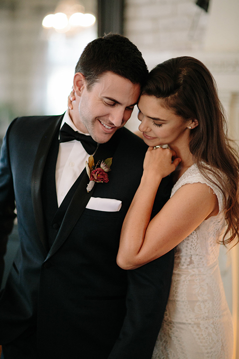 Southern-california-wedding-at-the-ebell-of-long-beach-bride-and-groom-hugging-close-up-bride-wearing-a-lace-a-line-dress-with-straps-and-hair-in-loose-down-waves-and-groom-in-navy-tux-with-black-trim-and-black-bowtie