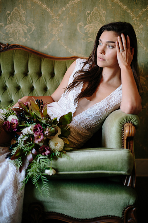 Southern-california-wedding-at-the-ebell-of-long-beach-bride-lace-gown-sitting-with-bouquet-bride-wearing-a-lace-a-line-dress-with-straps-and-hair-in-loose-down-waves-holding-her-bouquet-and-looking-off-to-the-side-and-her-hand-resting-on-her-head