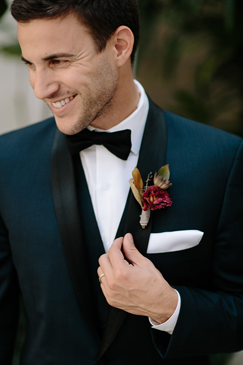 Southern-california-wedding-at-the-ebell-of-long-beach-groom-navy-tuxedo-close-up-groom-in-navy-tux-with-black-trim-and-black-bowtie-with-a-white-pocket-square-and-burgundy-boutionniere