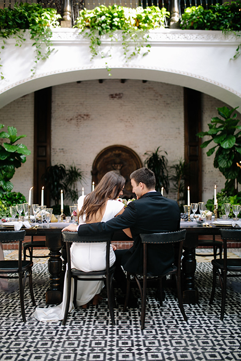 Southern-california-wedding-at-the-ebell-of-long-beach-reception-bride-and-groom-sitting-at-table-bride-wearing-a-lace-a-line-dress-with-straps-and-hair-in-loose-down-waves-and-groom-in-navy-tux-with-black-trim-and-black-bowtie