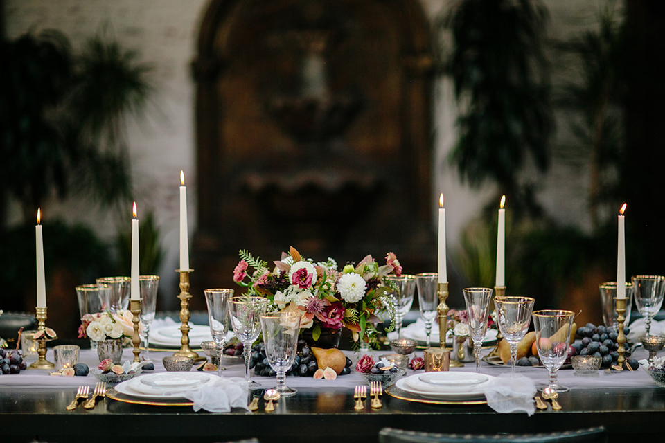 Southern-california-wedding-at-the-ebell-of-long-beach-table-set-up-with-flowers-wooden-table-and-chairs-with-neutral-colored-linneds-and-high-roman-candles-with-green-andwhite-florals